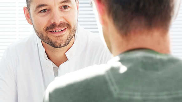 Arzt im Gespräch mit einem Patienten in hell ausgeleuchtetem Raum