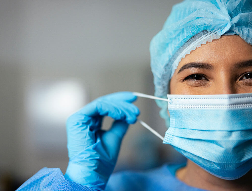 Gesicht einer lächelnden Chirurgin mit OP-Maske und blauen Handschuhen