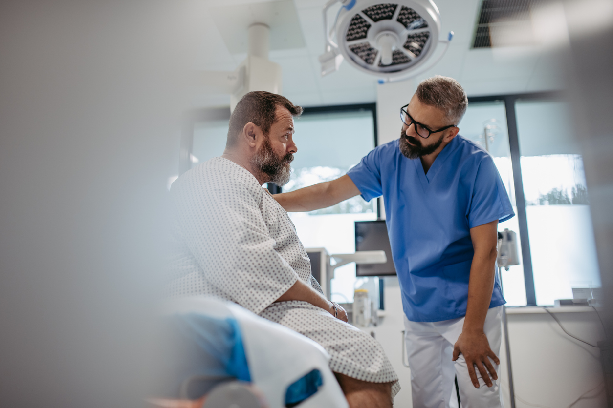 Arzt spricht beruhigend mit einem Patienten im Krankenhauskleid im Behandlungsraum