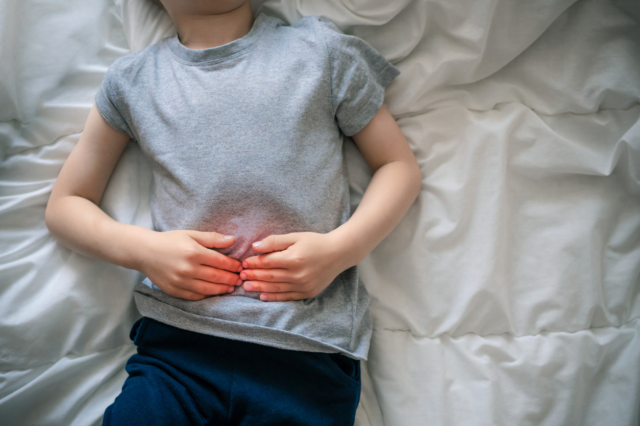 Kind liegt im Bett und hält sich den Bauch vor Schmerzen